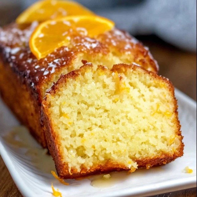 Orange glaze pound cake on a wire rack with white glaze drizzled down the sides, golden buttery loaf cake with tight crumb, fresh orange zest on top, slice cut showing moist interior