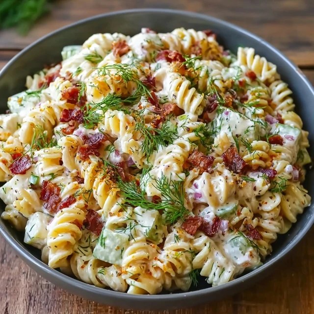 Creamy pasta salad with bacon in a white serving bowl, bowtie pasta coated in creamy ranch dressing, crispy bacon bits, halved cherry tomatoes, shredded cheddar, sliced green onions, fresh dill on top