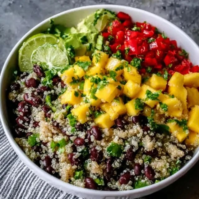 Quinoa black bean mango salad in a large serving bowl, fluffy white quinoa, black beans, bright orange mango cubes, red bell pepper, red onion, fresh cilantro, lime wedges, drizzle of dressing on top, summery natural light